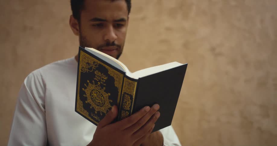 Man with white shirt and beard reads quran