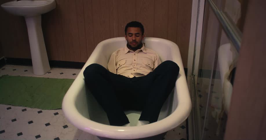 Man with beard white shirt and black pants lies in bathtub in the bathroom