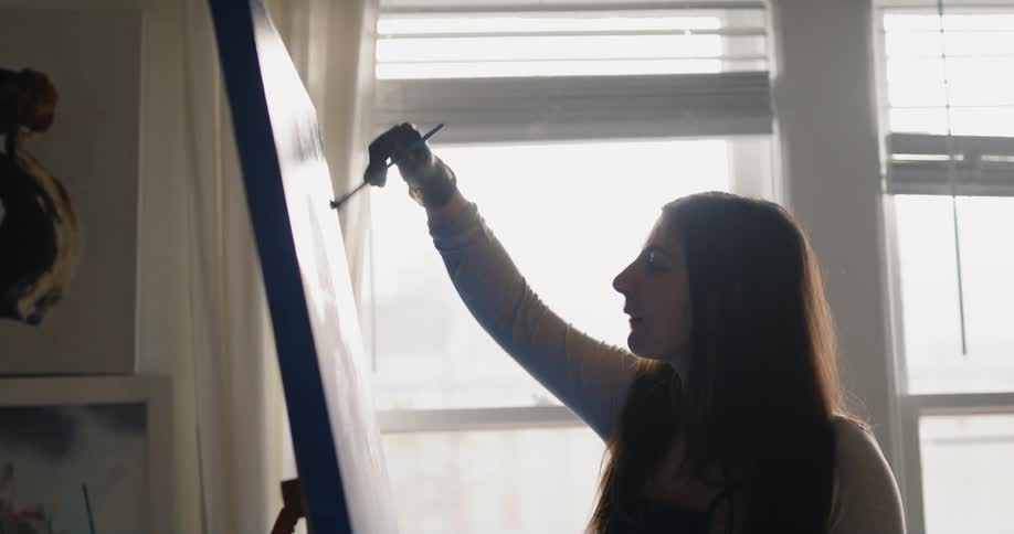 An artist paints on a large canvas indoors during the day