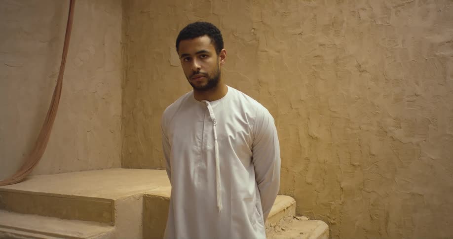 Man with beard and a thawb stands in front of stairs