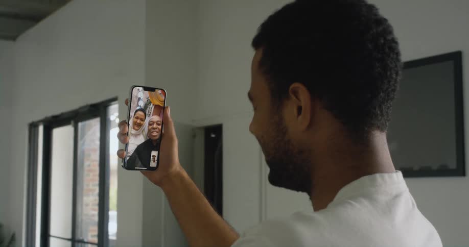 A man laughs while chatting with two women on a video call at home on his smartphone