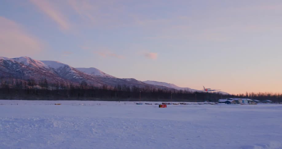 A small plane takes off from a snow covered rural airport near mountains