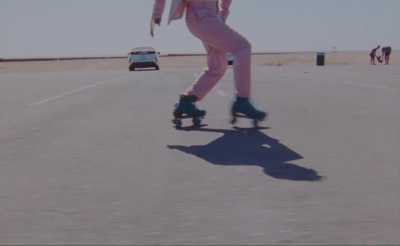 Person in pink pants dancing in blue roller skates across parking lot at the beach