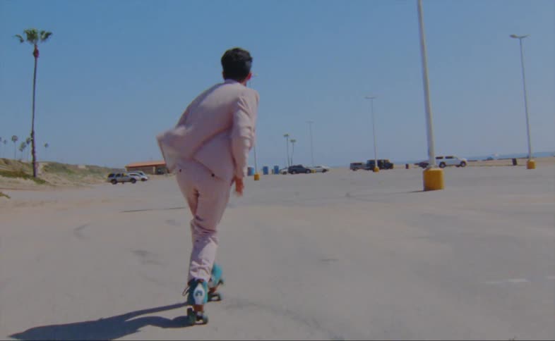 A man wearing a pink jacket and pants is dancing on roller skates in a parking lot