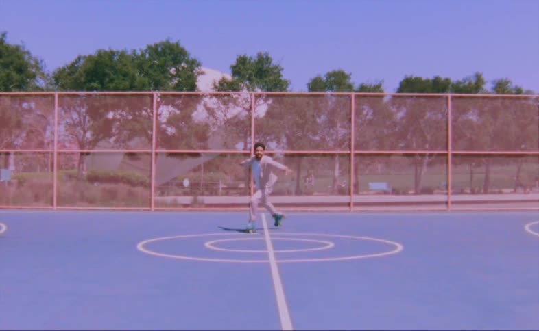 A man wearing a pink jacket and pants is dancing on roller skates on an outdoor basketball court