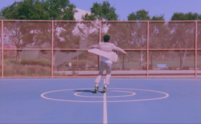 Man dances on roller skates on sports court in park on sunny day