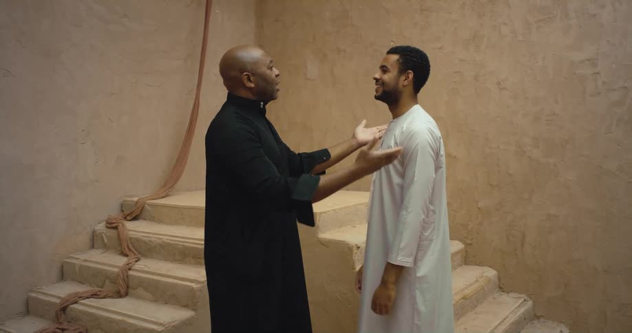 A priest taps a young man on both shoulders as they talk