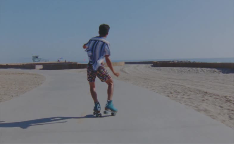 A man dances while roller skating along a path through a beach on a sunny day