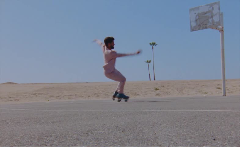 A man wearing a pink jacket and pants is roller skating on an outdoor basketball court and he loses his balance and quickly gets back up
