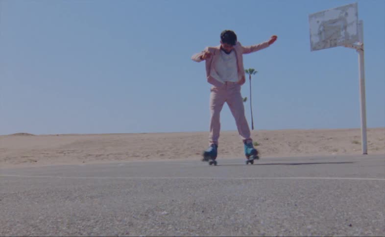 A man wearing a pink jacket and pants is dancing on roller skates on an outdoor basketball court