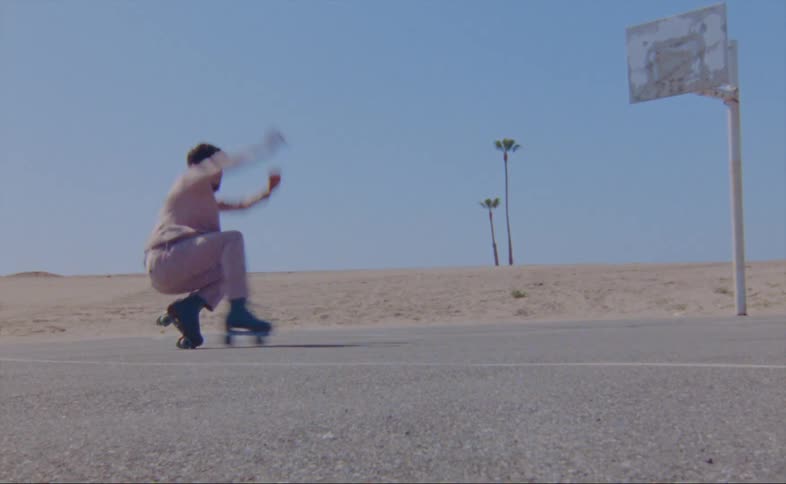 A man wearing a pink jacket and pants is roller skating on an outdoor basketball court and he does the russian dance