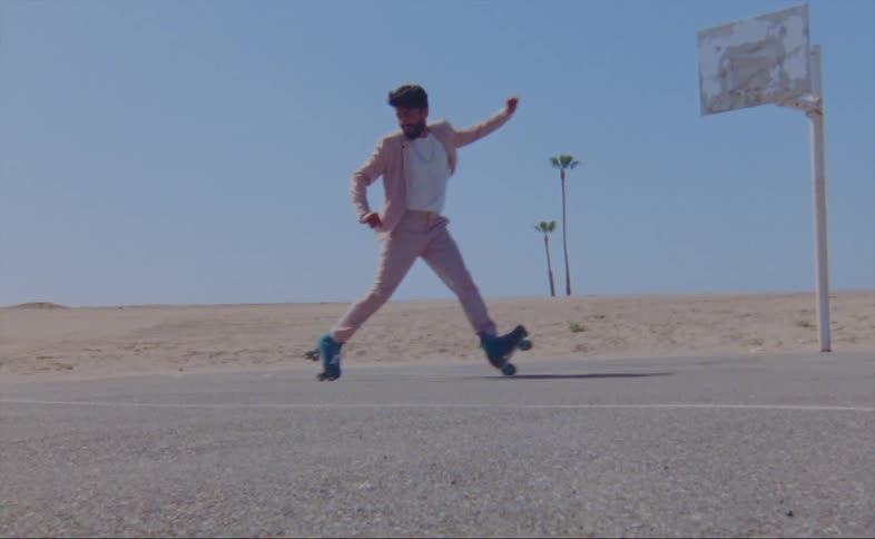 A man wearing a pink jacket and pants is dancing on roller skates on an outdoor basketball court