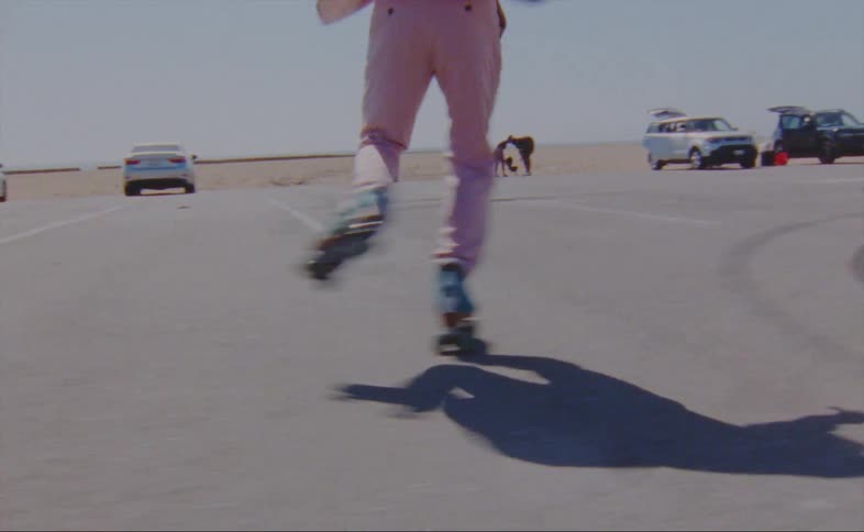 A man roller skates and dances through a parking lot at the beach