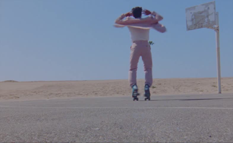 Man dances on roller skates on basketball court bordered by sand