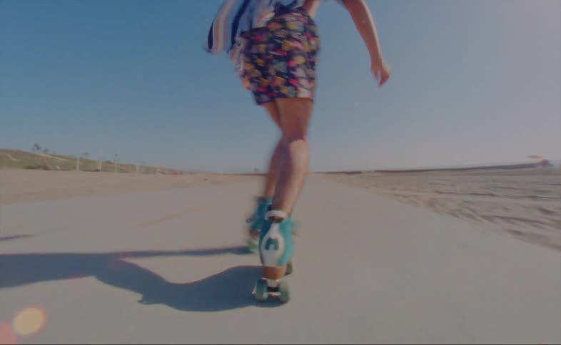 A man wearing shorts and a striped shirt is roller skating on a road at the beach
