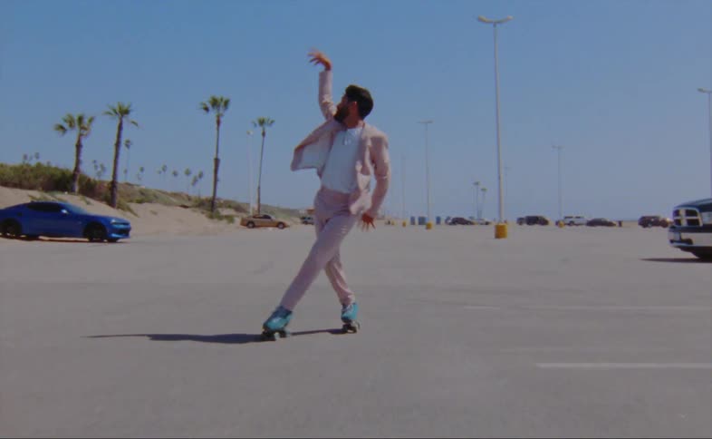 A man wearing a pink jacket and pants is dancing on roller skates in a parking lot