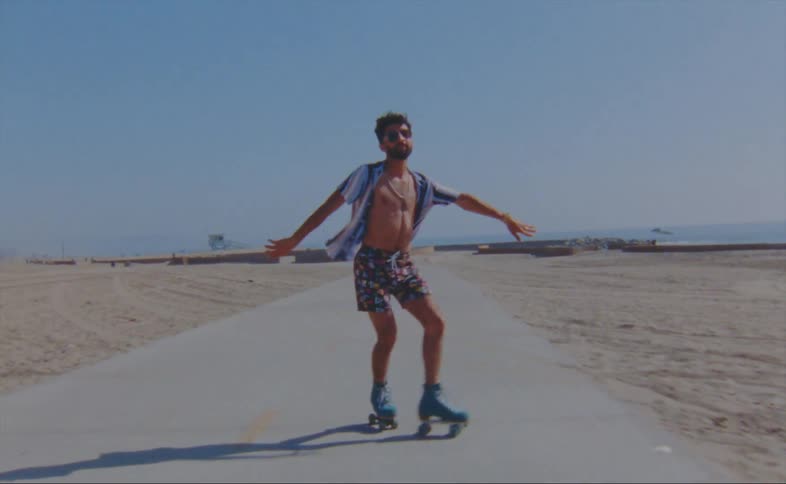 A man wearing shorts and a striped shirt is dancing on roller skates on a road at the beach