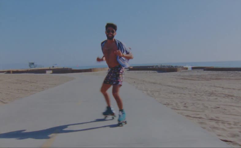 A man dances while roller skating along a pathway on a beach on a clear day