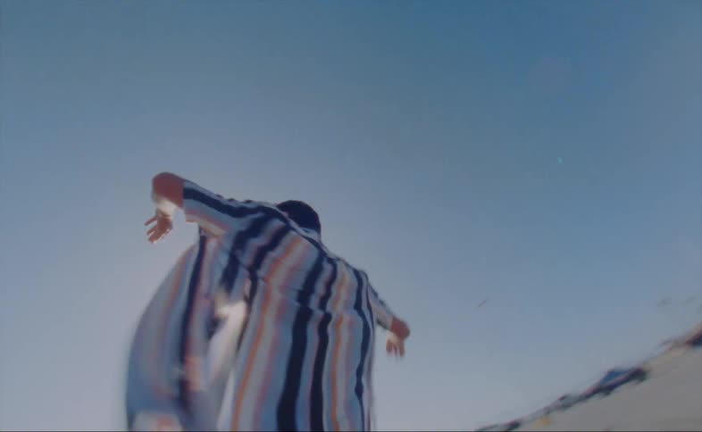 A man with his shirt open twirls and dances in the sunshine near the beach