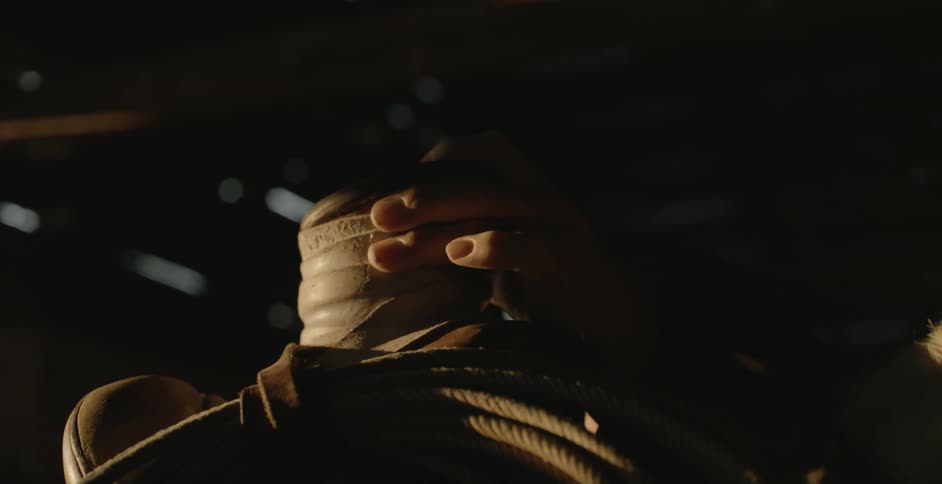 A man in a barn puts a saddle on a horse
