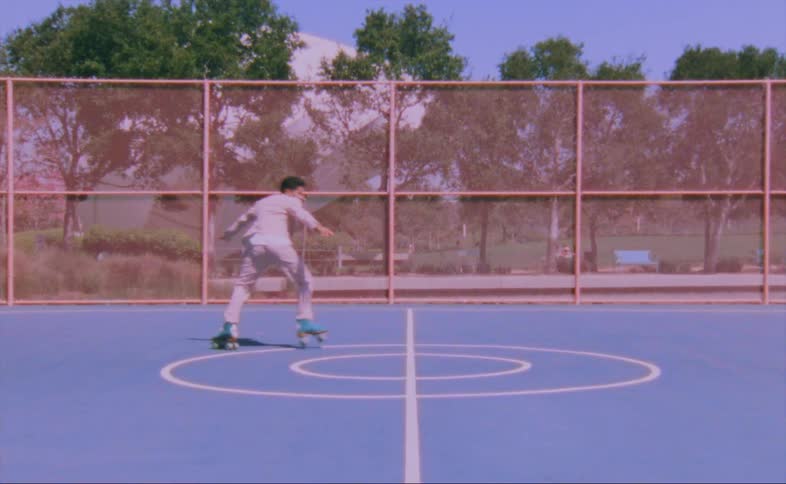 Man in tan suit roller skating in basketball court outdoors