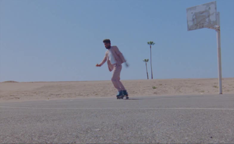 A man wearing a pink jacket and pants is dancing on roller skates on an outdoor basketball court