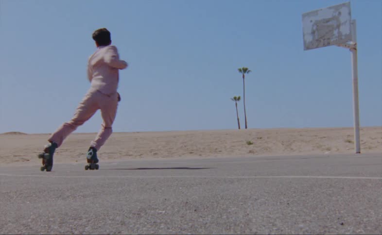 A man dances on roller skates in a parking lot near an abandoned basketball hoop