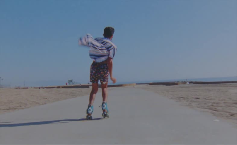 A man wearing shorts and a striped shirt is dancing on roller skates on a road at the beach