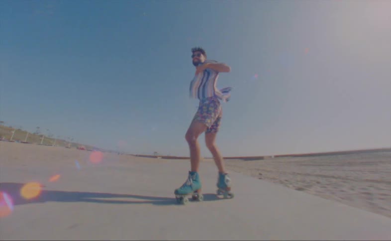 A man dances while roller skating along a path on a public beach on a sunny day