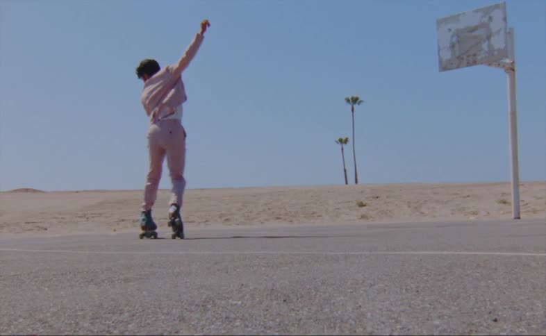 A man dances in roller skates on an outdoor basketball court during a clear day