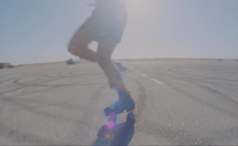 A man wearing blue skates and colorful print shorts twirling and dancing as he roller skates in the sunshine