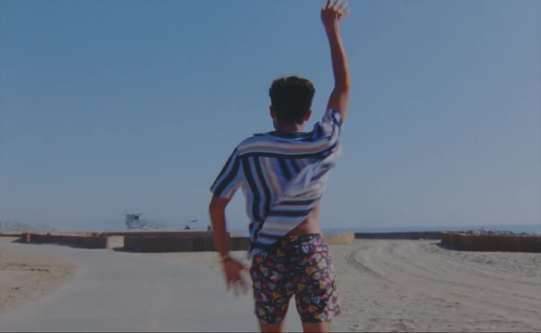 A young man roller skates and dances next to a beach