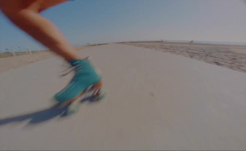 A man slips and falls while roller skating backwards along a path on a beach on a sunny day