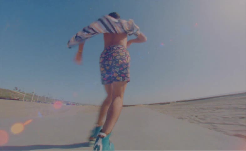 A man wearing shorts and a striped shirt is dancing on roller skates on a road at the beach