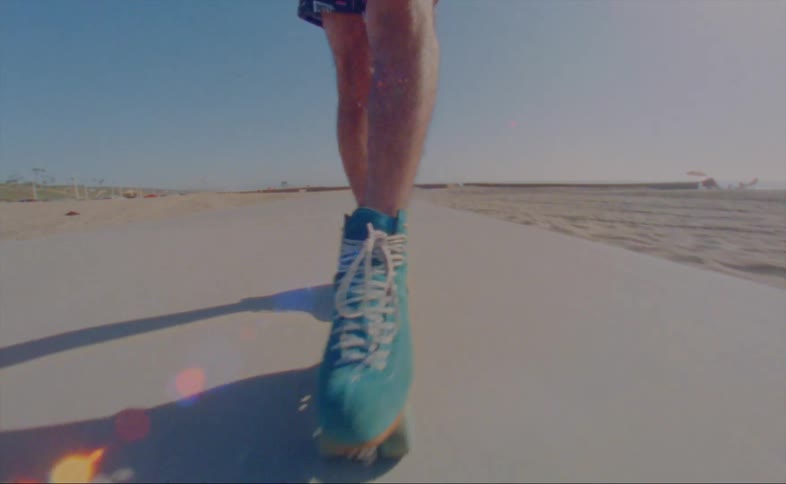 A man wearing shorts is skating backwards doing cross cuts on a road at the beach