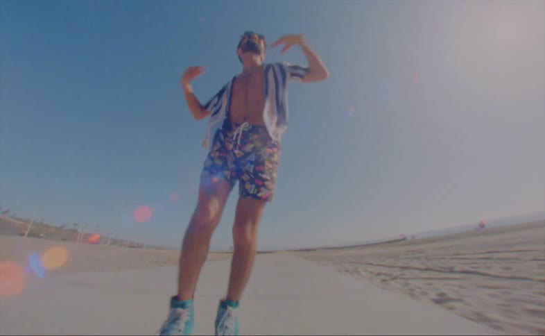 A man dances while roller skating backwards along a path on a beach during the day