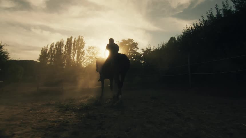 A man rides a horse through a corral in a rural area during the day