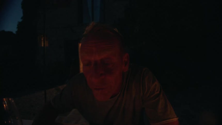A man leans forward to out the candles after taking a big sip from his wine glass