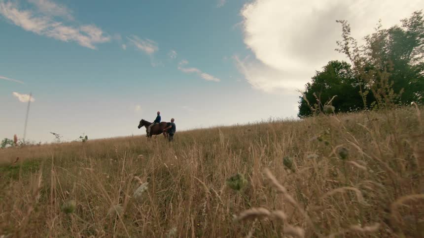 Man walks down to man on horse on grassy hill slope