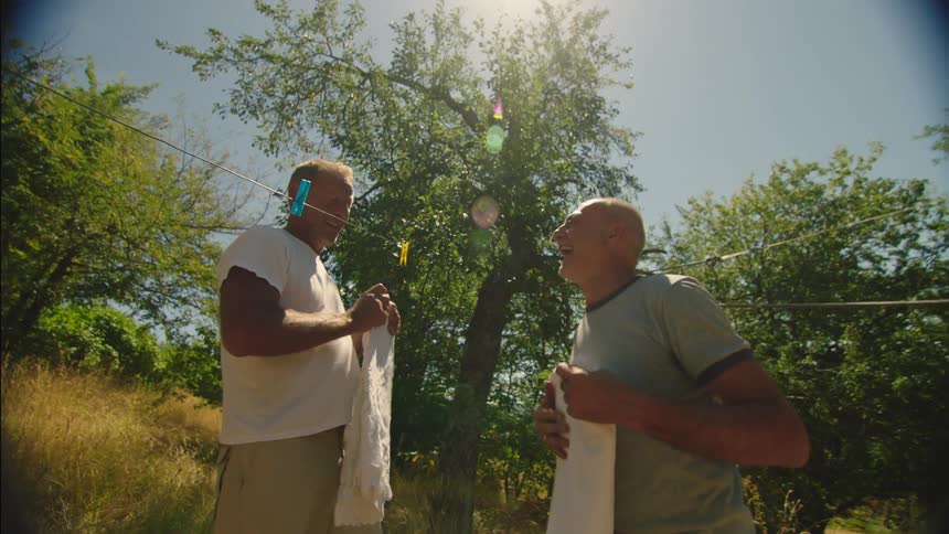 Two men are laughing as they remove clothes from the line