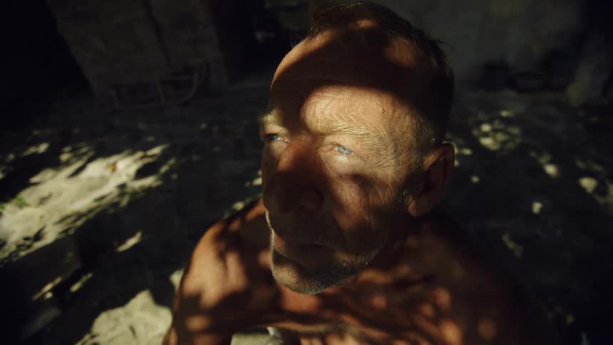 A man looks up into the sunlight through the trees and prays