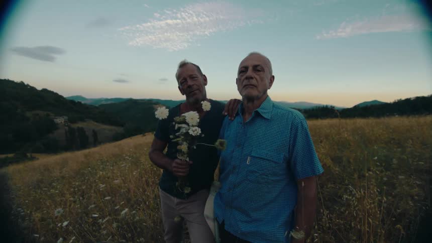A pair of men look into the camera while standing on a hill in the countryside during the day