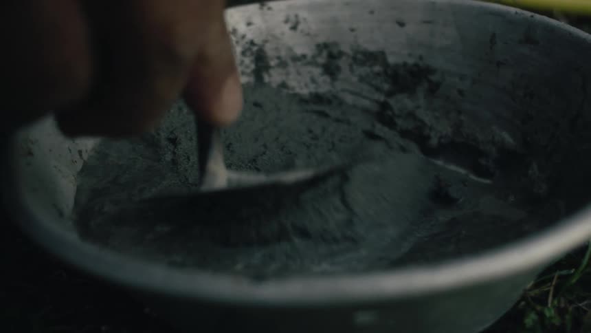 Mixing cement into a paste in a round metal bowl with small spatula
