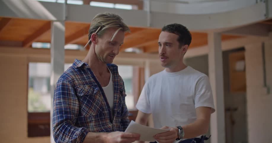 A pair of men talk while referencing a sheet of paper and gesturing around at their surroundings