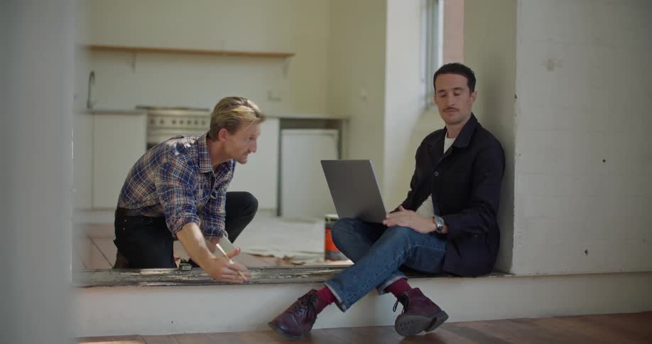 A man uses his laptop as he talks with someone in the empty room