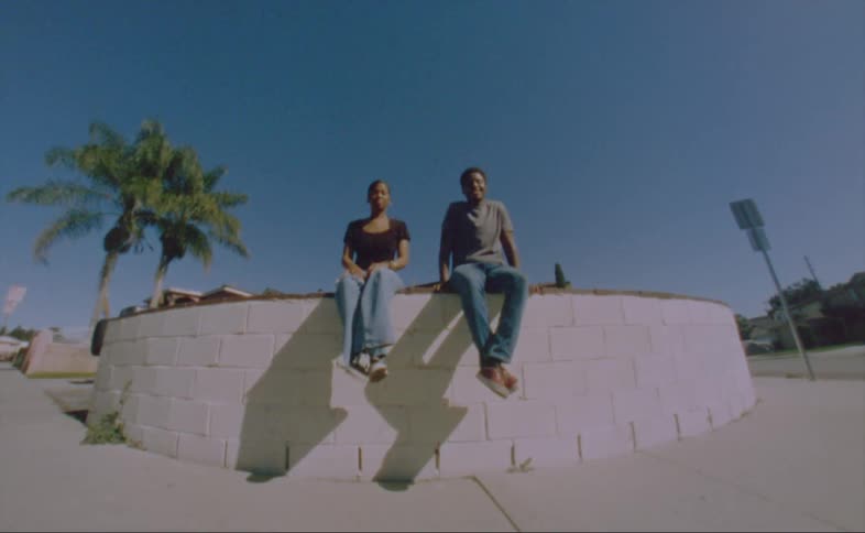 Man whit gray shirt and jeans sits next to woman wearing black shirt and jaens on the wall