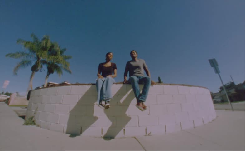 A man and woman adjust themselves while sitting on a rounded ledge in a neighborhood