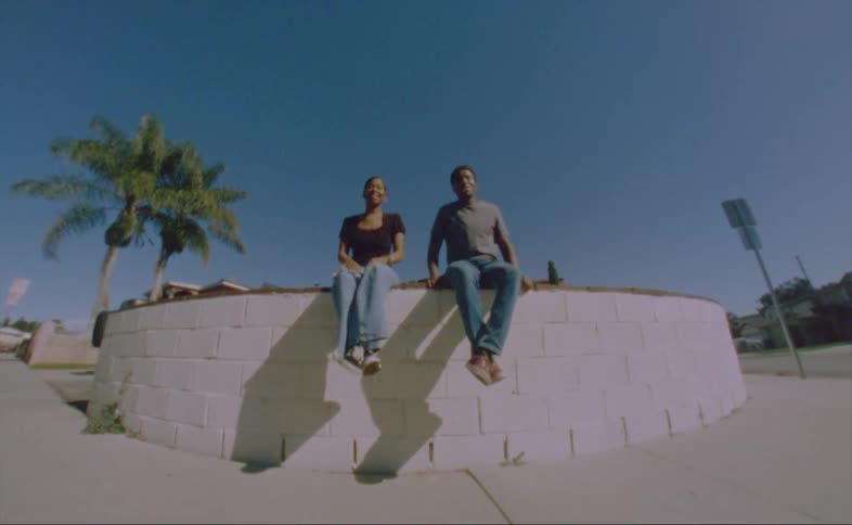 Man with gray shirt jeans and woman wearing black shirt and jeans sits on wall talk with one another
