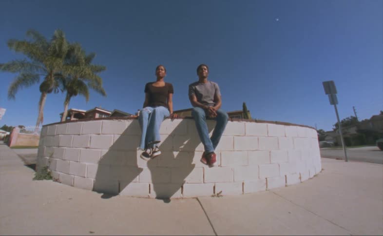A man and woman sit on a rounded ledge in a neighborhood