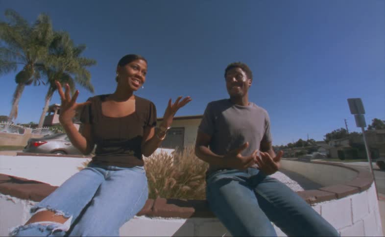 Man in black shirt and jeans talks with woman with black shirt and jeans sitting on wall